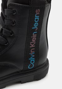 Czarne skórzane botki z fakturowaną powierzchnią, sznurowane, z boczną panelą z wielokolorowym logo "Calvin Klein Jeans". Gumowa podeszwa.