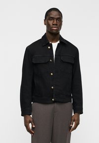 Μαύρο τζιν μπουφάν με δύο μπροστινές τσέπες, κλείσιμο με κουμπιά και χρυσές λεπτομέρειες. Διαθέτει κλασική γραμμή και υφή φινιρίσματος.