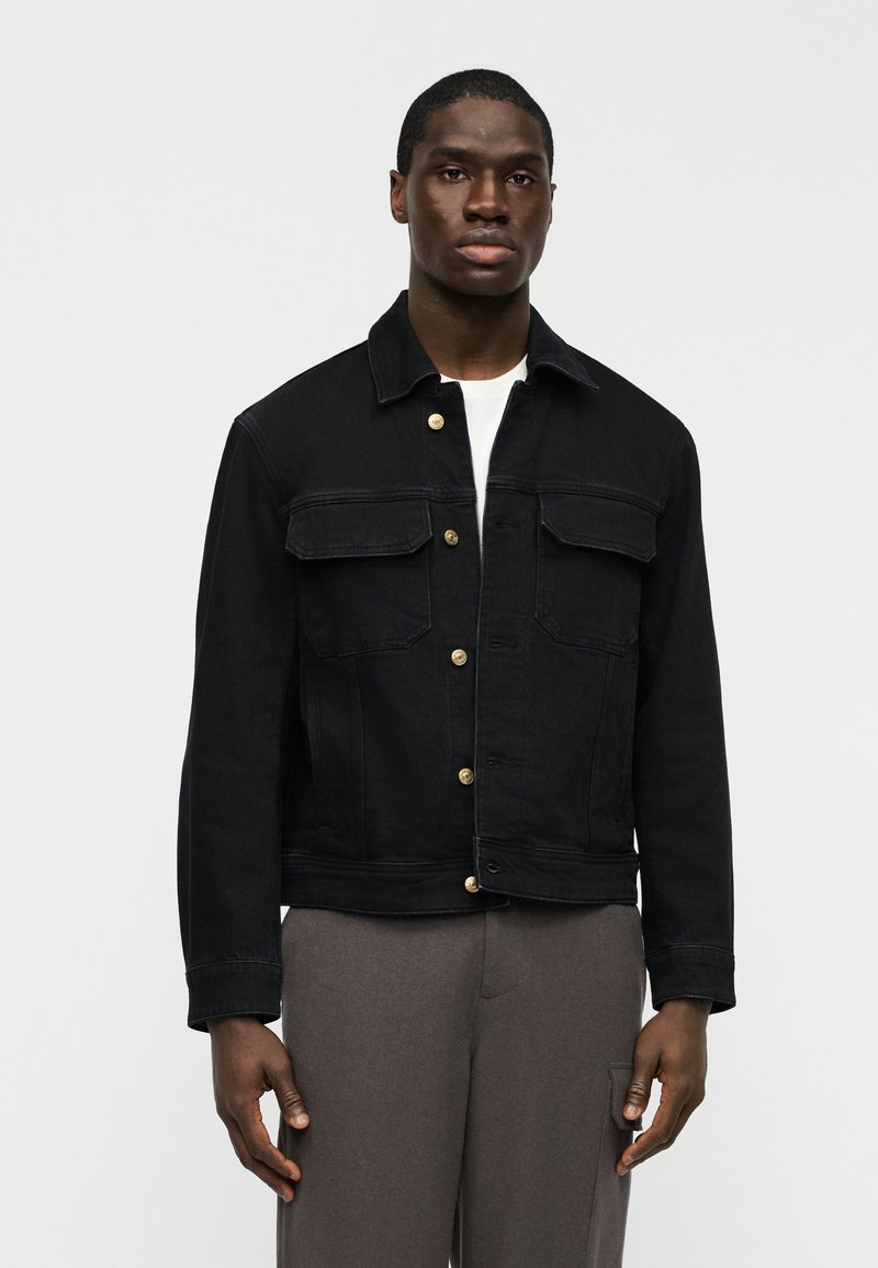 Μαύρο τζ ιν μπουφάν με δύο μπροστινές τσέπες, κλείσιμο με κουμπιά και χρυσές λεπτομέρειες. Διαθέτει κλασική γραμμή και υφή φινιρίσματος.