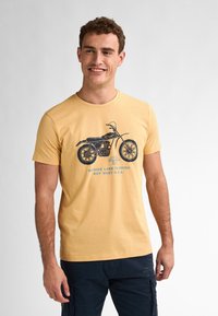 Žluté bavlněné tričko s modrou grafikou motorky a textem: "Bayside Lane Florida Key West USA." Krátké rukávy a kulatý výstřih.