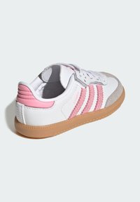 Biało-różowy sneaker z trzema różowymi paskami, zamszowym noskiem i gumową podeszwą. Posiada sznurowanie oraz wyściełany kołnierz.