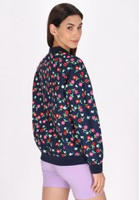 Bloemen bomberjack in marineblauwe stof, met levendige bloemen in pink, wit en groen. Ribgebreide manchetten en tailleband met een zachte textuur.