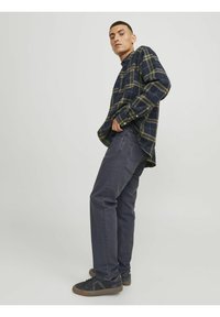 Camisa de franela en azul marino con cuadros verdes y amarillos, combinada con jeans gris oscuro y zapatillas negras, con un corte relajado y detalles de botones.