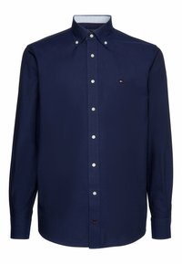 Camisa de botones de manga larga de color azul marino con botones blancos, cuello abotonado y pequeño logo de Tommy Hilfiger en el lado izquierdo del pecho.