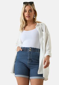 Jeansshorts med hög midja och två framknappar, med uppvikta kantlinjer; kombinerat med en vit linne och en överdimensionerad vit skjorta.