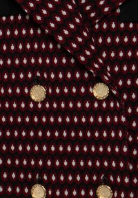 Tissu à motifs rouges et noirs avec des formes de gouttes blanches et quatre boutons dorés texturés disposés en deux rangées.