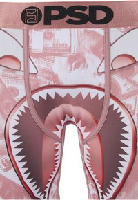 Close-up van rozenkleurige PSD-boxershorts met het PSD-logo, voorzien van een haaienbekgrafiek en een vage achtergrond van geldbiljetten.