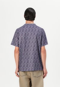 Krátky rukáv, fialová vzorovaná košeľa s opakujúcim sa motívom siluety, vyrobená z ľahkej látky s okrúhlym výstrihom.