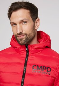 Rote Daunenjacke mit Kapuze, mit horizontal gestepptem Design, schwarzem Frontreißverschluss und CMPD CAMP DAVID-Logo auf der linken Brust.