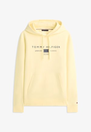 Jasnożółta bluza z kapturem Tommy Hilfiger z przednią kieszenią, kapturem ze ściągaczem oraz napisem "American Classics" z logo i "EST. 1985" na piersi.