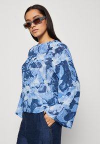 Top lungo a maniche, blu floreale, con scollatura rotonda e vestibilità comoda. Il tessuto presenta un motivo testurizzato, abbinato a pantaloni in denim blu.
