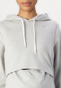 Hoodie cropped cinza claro feito de material macio, com um bolso frontal, cordões ajustáveis brancos e um design de ajuste relaxado.