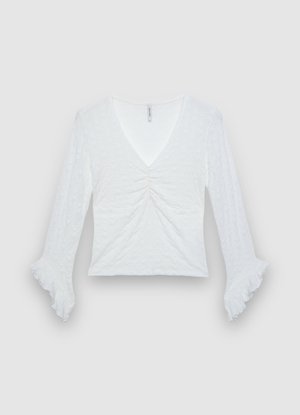 Haut blanc à manches longues avec encolure en V, fronces au centre, et poignets évasés. Confectionné en tissu texturé, avec un design léger.