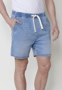 Heled sinised teksapüksid lühikesed, elastse vöökohaga, paelaga sulgemise ja küljetaskutega. Pehme tekstuur ja juhuslik disain.