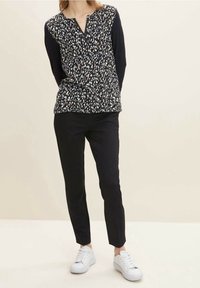 Langarmhemd mit einem schwarzen gemusterten Vorderteil und einfarbigen schwarzen Ärmeln, kombiniert mit schwarzen Slim-Fit-Hosen und weißen Sneakers.