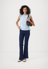 Top de tirantes de encaje azul claro con bordes en forma de concha, jeans acampanados azul oscuro y bolso negro. La modelo lleva unos planos beige con detalles en negro.