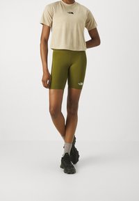 Beige kortärmad t-shirt med logotyp, olivgröna cykelbyxor, grå strumpor och svarta träningsskor. Enkelt mönster och figurnära snitt; minimala detaljer.