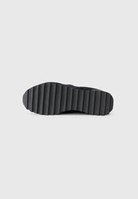 Semelle de chaussure en caoutchouc noir avec une texture nervurée et un texte de marque en relief, présentant une base plate et des bords distincts et lisses.