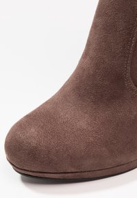 Botín de ante marrón con punta redondeada, textura suave y una ligera plataforma. Detalle de costura notable a lo largo de las costuras.