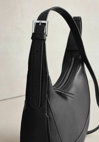 Černá kožená taška s texturovaným povrchem, jedním nastavitelným popruhem s kovovou sponou a kapsou na zip.