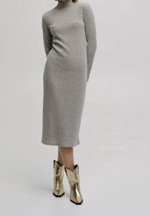 Robe en maille côtelée grise avec des manches longues et un col montant, associée à des bottes métalliques dorées jusqu'aux chevilles avec un bout pointu et un style cowboy.