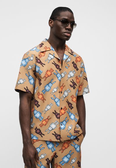Πουκάμισο με κοντά μανίκια κατασκευασμένο από ελαφρύ ύφασμα με καφέ φόντο. Διαθέτει πολύχρωμο, επαναλαμβανόμενο σχέδιο με λαγουδάκια και σακίδια σε μπλε, πορτοκαλί και μαύρο χρώμα.