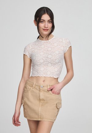 Top corto in pizzo bianco con maniche corte e orlo scallopato. Gonna in denim beige con tasche anteriori e tasche laterali cargo.