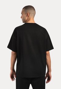 Camiseta de algodón negra de corte oversize con escote redondo, mangas cortas y un ajuste relajado. La tela parece suave con un acabado mate.