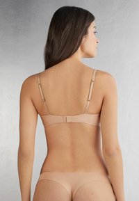 Nude naadloze beha met verstelbare bandjes en haak-en-oogsluiting, voorzien van zachte stof en een minimalistisch ontwerp voor comfort en veelzijdigheid.
