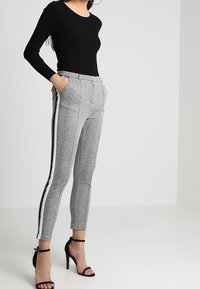 Šedé kalhoty na míru s černými bočními pruhy, strukturální látka, slim fit, přední kapsy, spárované s černým dlouhým rukávem a černými podpatky.