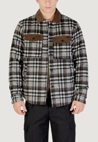 Giacca camicia in flanella a quadri neri, bianchi e marroni con colletto in cotone a coste e due tasche sul petto con bottoni. Dotata di chiusura a scatto.