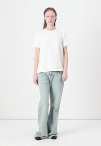 Hvid t-shirt med korte ærmer kombineret med lyseblå bredde bukser og sorte sko. Stoffet ser glat ud, med et simpelt design og afslappet pasform.