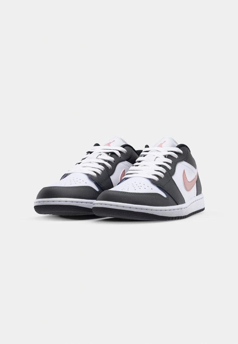 Zapatillas deportivas en blanco y negro con acentos en rosa, que presentan una parte superior de cuero suave, punta perforada y suela de goma. Cuerdas blancas y marca visibles.