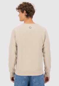 Beige crewneck sweatshirt met geribde manchetten en zoom, voorzien van een circulair logo detail op de achterzijde van de hals en een ontspannen pasvorm.