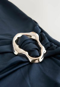 Tissu bleu marine présentant un design tordu avec un accent en métal argenté texturé et irrégulier au centre.