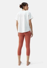 Balti medvilninė marškinė su trumpomis rankovėmis, su išblukusiu teksto dizainu ant nugaros. Suderinta su rudai oranžinėmis, iki kelių siekiančiomis leggingais.