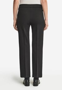 Svarta skräddarsydda byxor med ett slätt tyg, vid ben-design och en ren midja. Subtil veckdetalj längs framsidan.