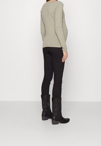 Haut gris texturé à manches longues associé à un pantalon noir ajusté et des bottes cowboy noires à talons, ornées de détails en relief et d'une fermeture éclair latérale.