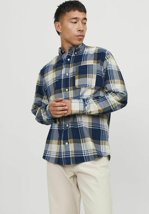 Camicia a quadri con una combinazione di colori blu navy, beige e verde oliva. Ha un design con bottoni, un colletto e una tasca sul petto.