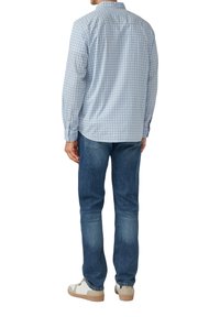 Blauw-wit geruite langemouwen shirt, van katoen, met knopenmanchetten, gedragen met donkerblauwe jeans en lichte sneakers.