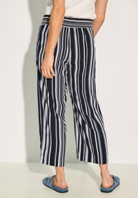 Randiga, marinblå och vita, vida byxor med smockad midja. Tyget verkar lätt och har en slät textur. Accentueras av en kortare längd.