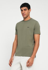 Olívazöld környakú rövid ujjú póló, pamutból készült, a mellrészen egy kis fekete "BOSS" logóval. Sima textúra, karcsúsított fazon.