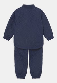 Navyblå vadderad jacka och byxor i set med geometriskt mönster, elastiska muddar och krage. Mjuk, vadderad textur för värme.