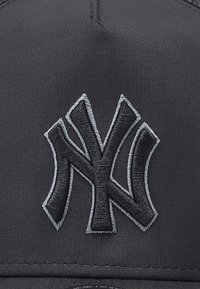 Casquette de baseball noire avec un logo "NY" gris brodé sur le devant. Le tissu a une texture lisse et mate, sans motifs supplémentaires.