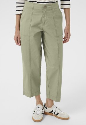 Light olive green cropped pants with a high waist, featuring large side pockets and a straight cut. Paired with white sneakers.
