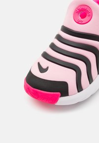 Rosa och svart sneaker med en slät ovandel, böjda linjer, rund logotyp-accent och en texturerad gummiyttersula med en rosa designdetalj.