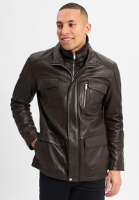 Braune Lederjacke mit einem Reißverschluss vorne, hohem Kragen und mehreren Taschen. Glatte Textur, taillierte Passform und detaillierte Nähte.