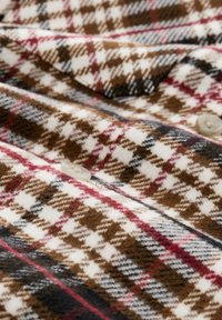 Braun, weiß und rot kariertes Gewebe mit einer weichen Textur, das große Karomuster und ein einzelnes Knopfdetail aufweist.