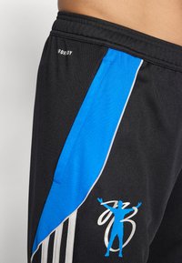 Juodos sportinės šortai su mėlynu šonu, baltais akcentų dryžiais ir mėlynu grafiniu logotipu, vaizduojančiu figūrą su pakeltomis rankomis.