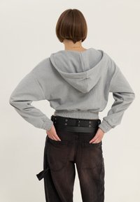 Felpa grigia corta con cappuccio, vita elastica e polsini a costine, abbinata a pantaloni neri a vita alta con tasche stile cargo e cintura.